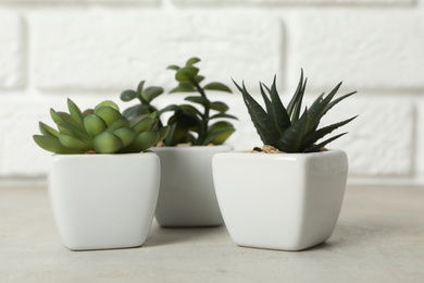 Photo of Beautiful artificial plants in flower pots on grey stone table near brick wall