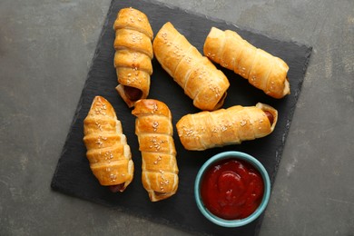 Photo of Delicious sausage rolls and ketchup on grey table, top view