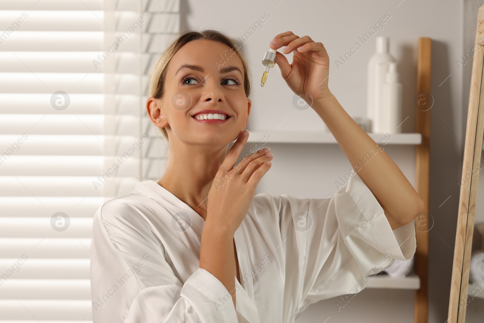 Photo of Beautiful woman with cosmetic serum in her hands in bathroom