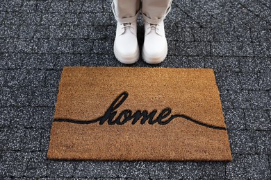 Photo of Woman in stylish boots near doormat with word Home on pavement, closeup