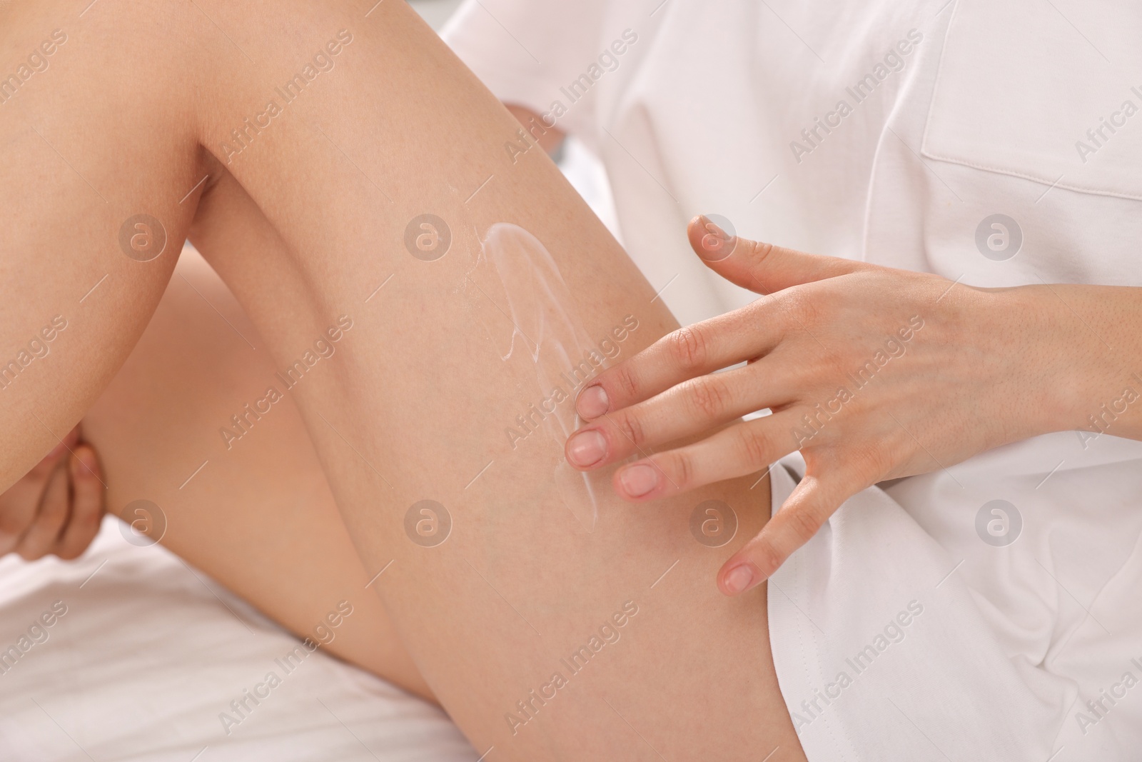 Photo of Woman applying cream onto leg in bed, closeup