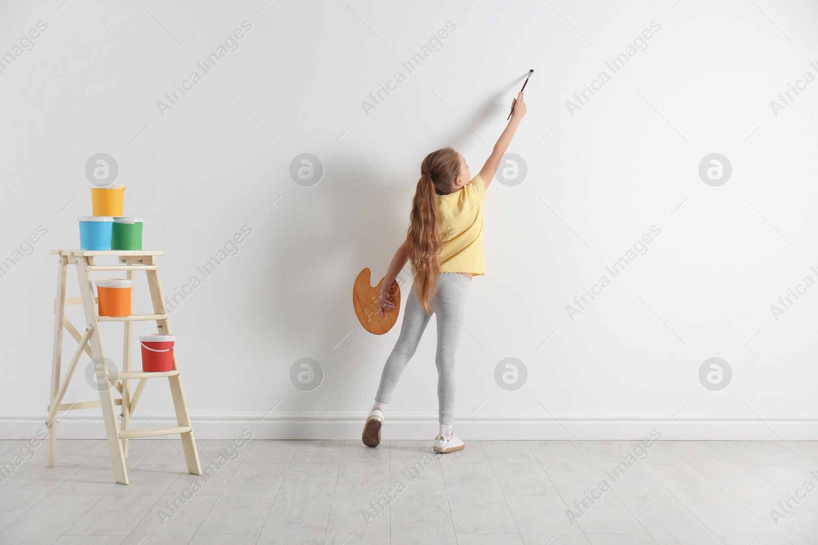 Photo of Little child painting on blank white wall indoors