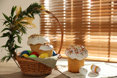 Photo of Traditional Easter cakes, dyed eggs and basket on wooden table indoors