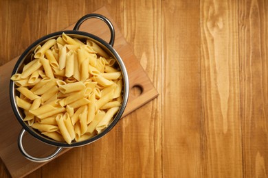 Cooked pasta in metal colander on wooden table, top view. Space for text