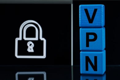 Photo of Acronym VPN (Virtual Private Network) made of light blue cubes on dark background with lock. Space for text