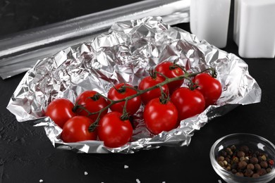 Tomatoes in aluminum foil and spices on dark textured table, closeup