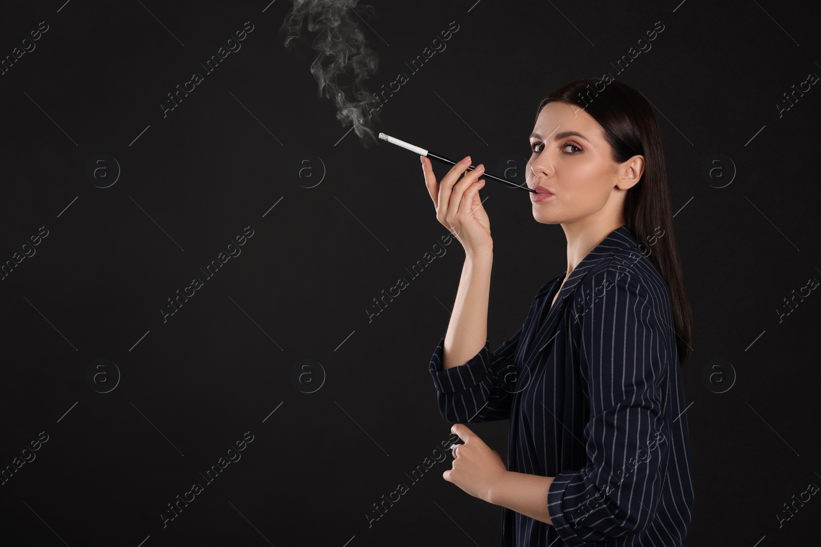 Photo of Woman using long cigarette holder for smoking on black background, space for text