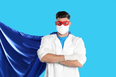 Photo of Doctor wearing face mask and cape on light blue background. Super hero power for medicine
