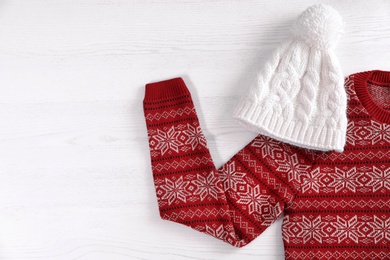 Photo of Knitted hat and Christmas sweater with pattern on wooden background, top view. Space for text