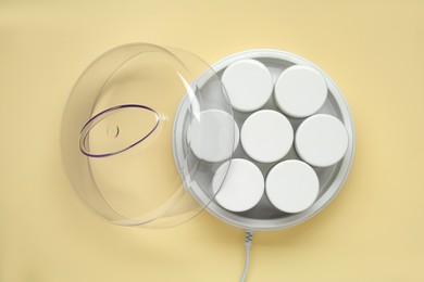 Photo of Modern yogurt maker with jars on beige background, top view