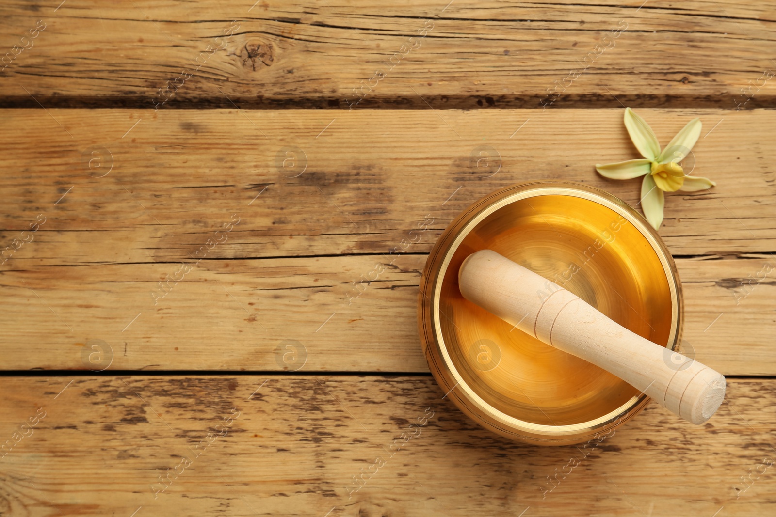 Photo of Golden singing bowl, mallet and flower on wooden table, flat lay. Space for text