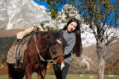 Young woman with horse in mountains on sunny day. Beautiful pet