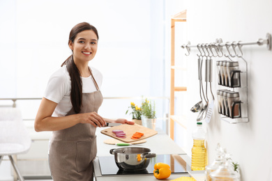 Young woman cooking tasty vegetable soup in kitchen