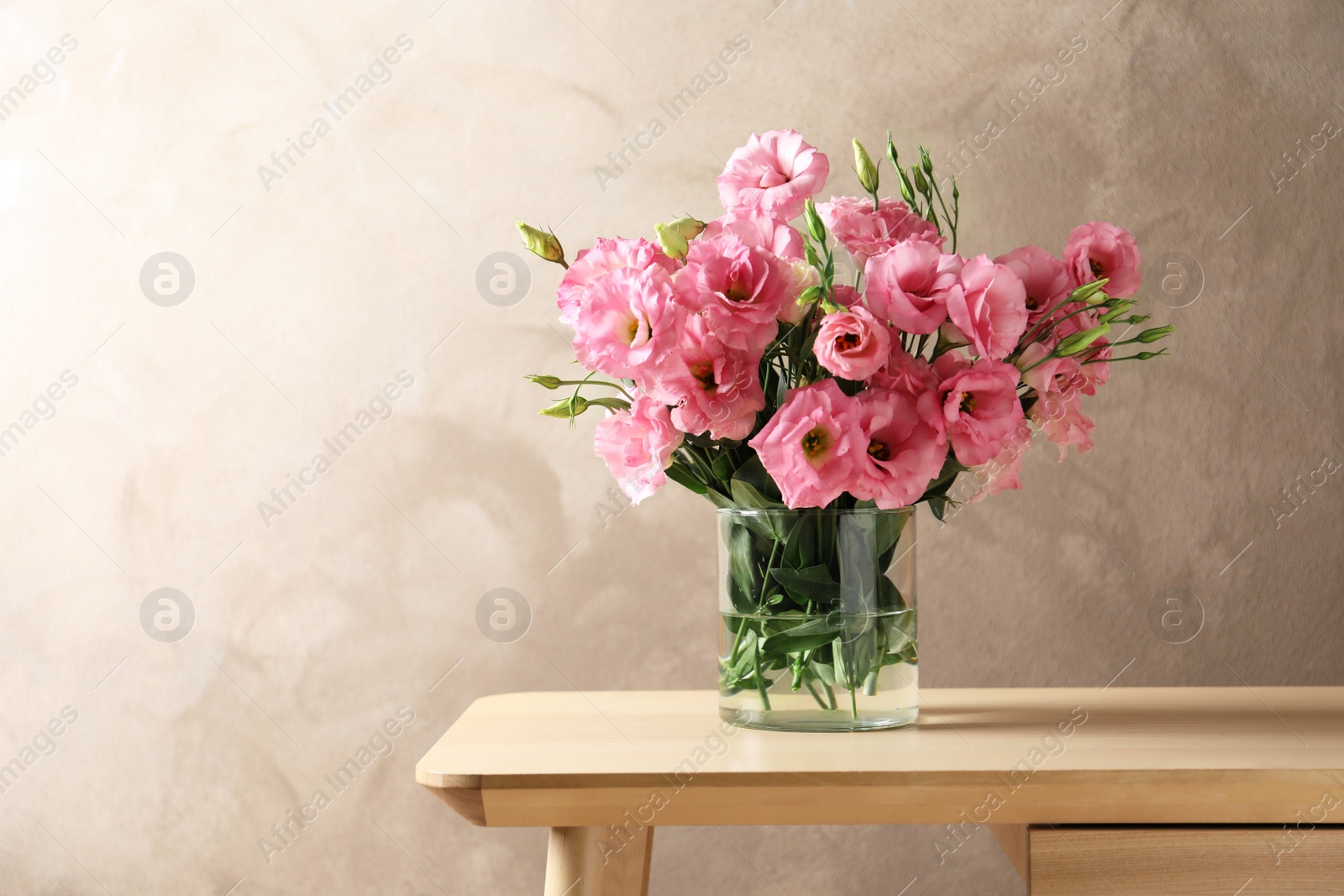 Photo of Vase with beautiful Eustoma flowers on table against color background