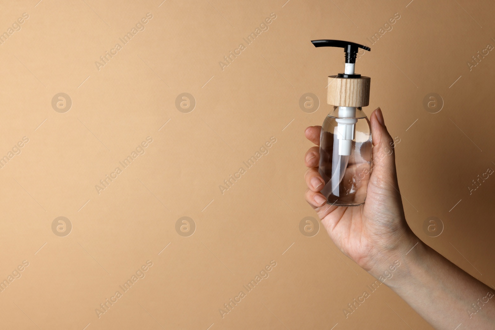 Photo of Woman holding bottle of cosmetic product on beige background, closeup. Space for text