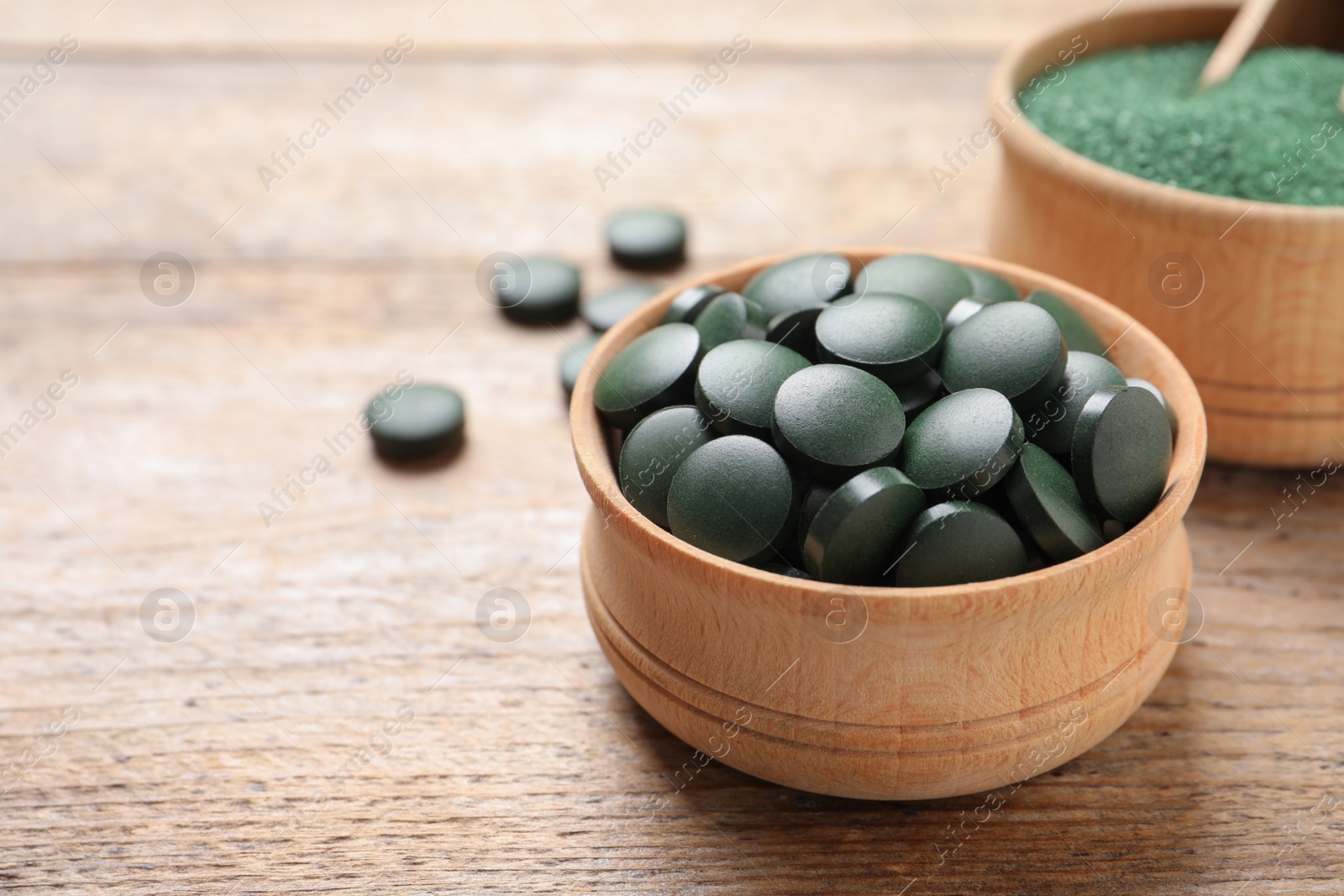 Photo of Bowls of spirulina pills and powder on wooden table, space for text