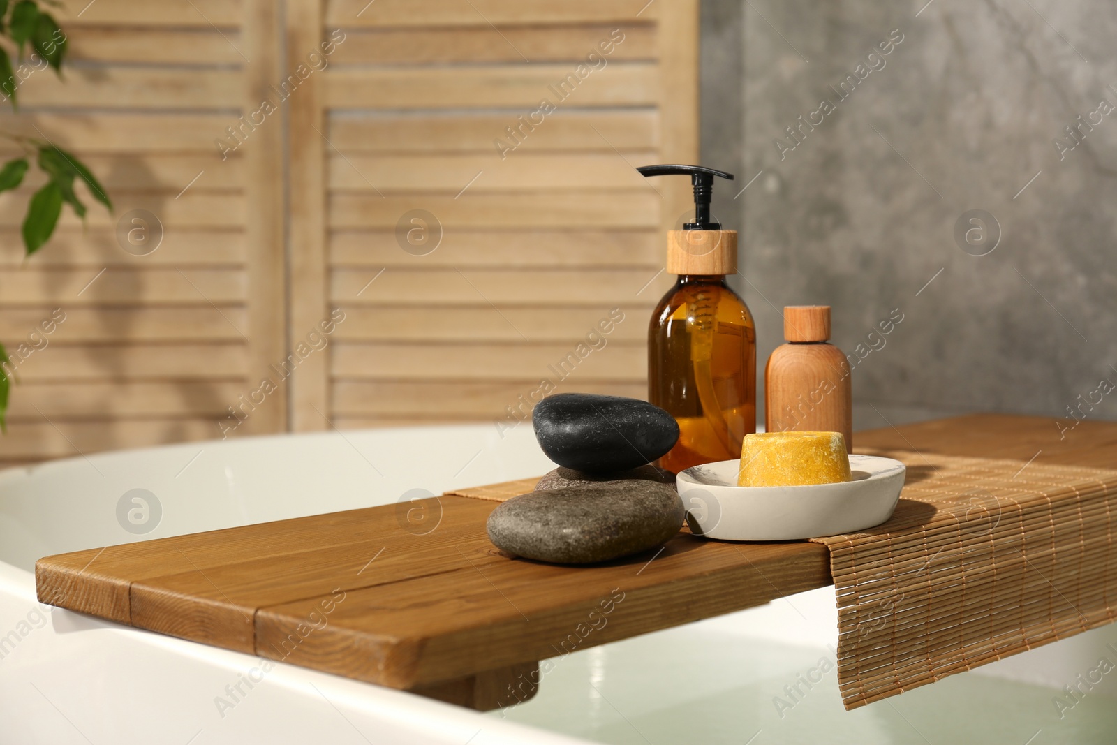 Photo of Wooden tray with spa products and stones on bath tub in bathroom. Space for text