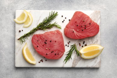Photo of Raw tuna fillets with peppercorns, lemon and rosemary on light gray table, top view