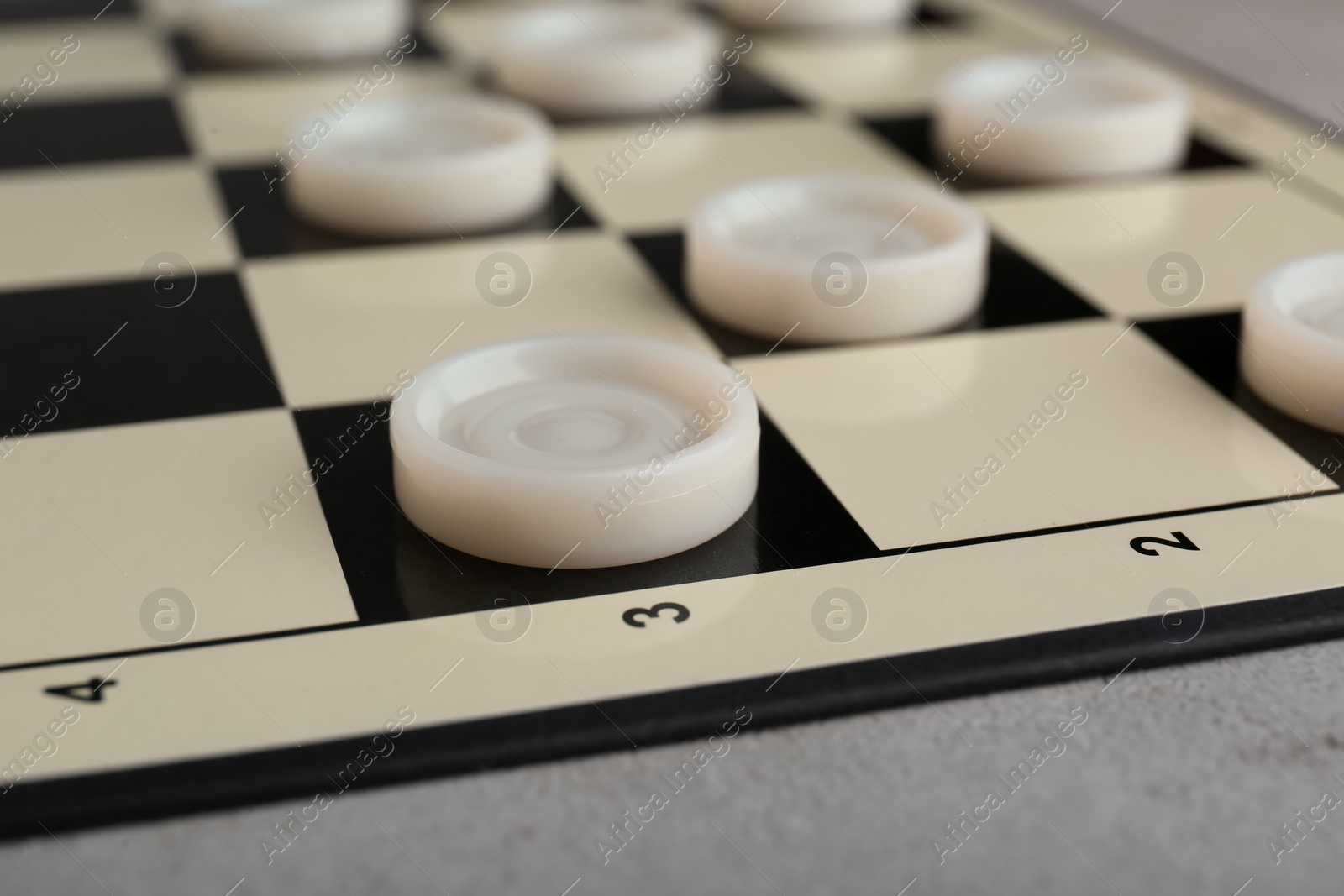 Photo of Checkerboard with game pieces on light grey table, closeup