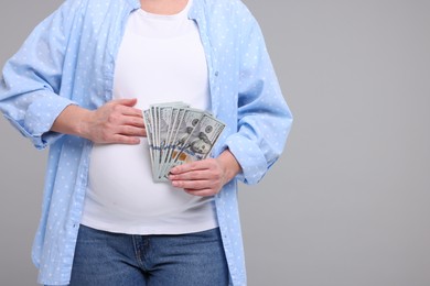 Photo of Surrogate mother. Pregnant woman with dollar banknotes on light grey background, closeup. Space for text