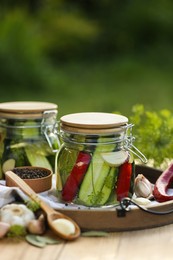 Photo of Jars of delicious pickled cucumbers and ingredients on wooden table against blurred background