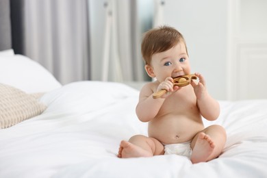 Cute baby boy with wooden rattle on bed at home. Space for text