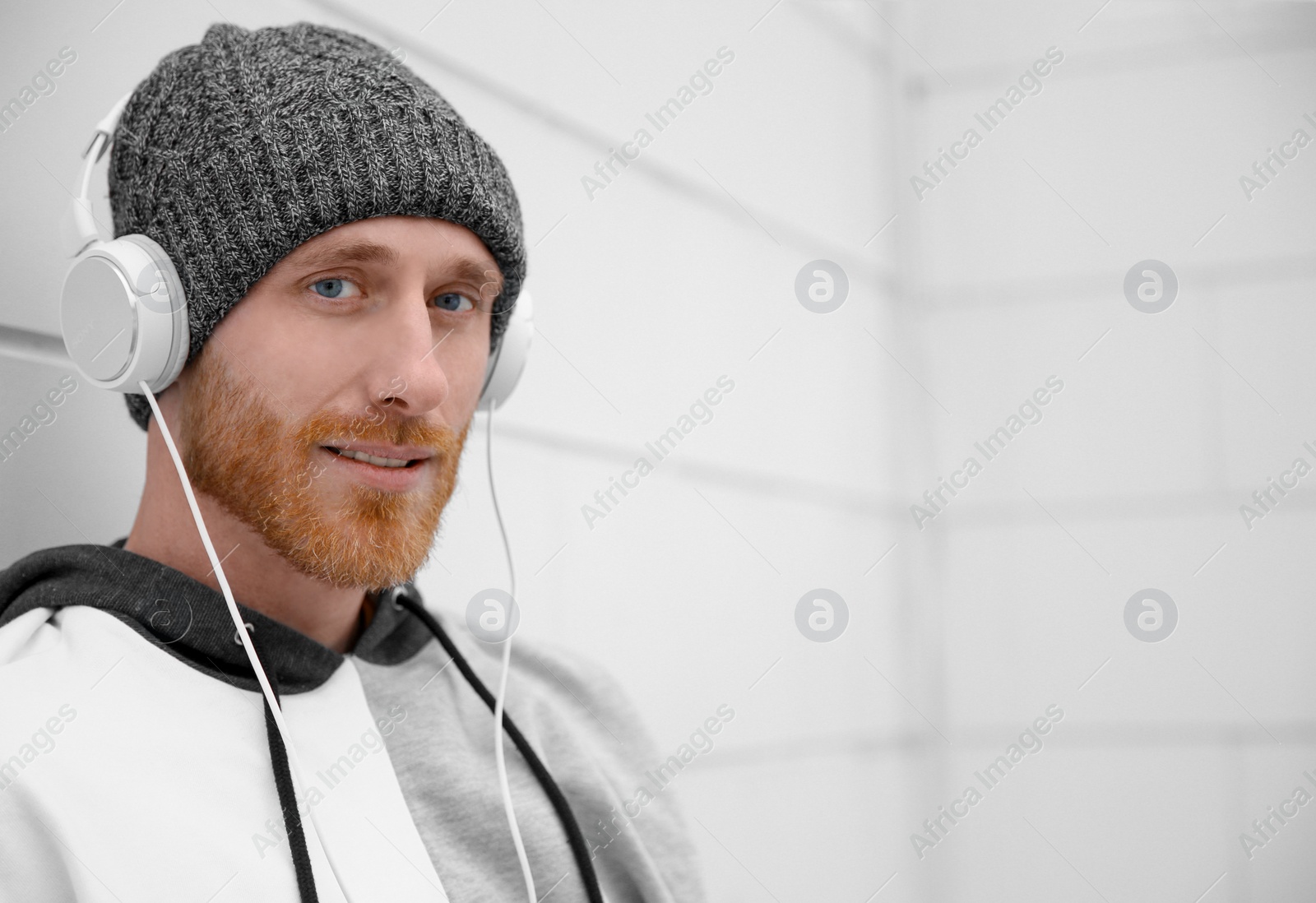 Photo of Young man listening to music with headphones near light wall. Space for text