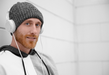 Young man listening to music with headphones near light wall. Space for text