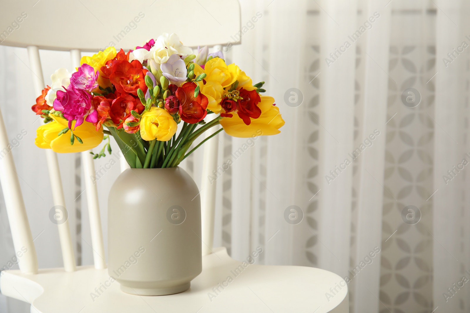 Photo of Vase with bouquet of spring freesia flowers on chair in room. Space for text