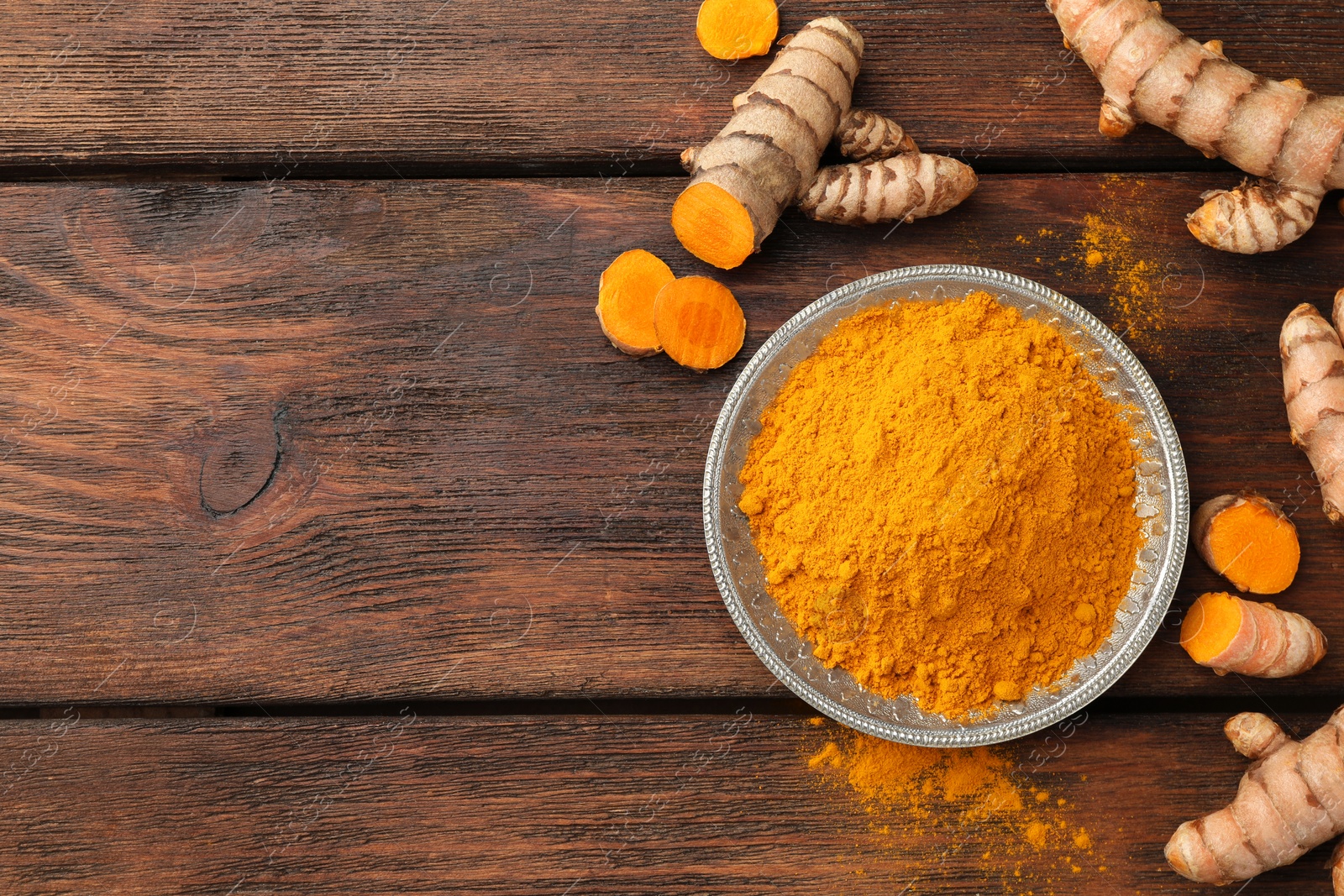 Photo of Plate with aromatic turmeric powder and cut roots on wooden table, flat lay. Space for text