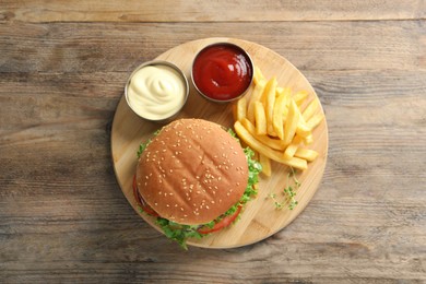 Delicious burger with beef patty, sauce and french fries on wooden table, top view