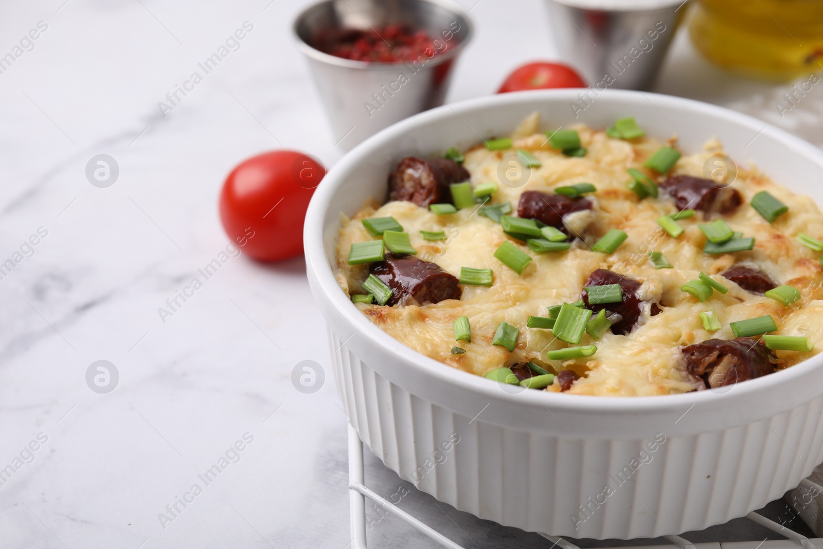 Photo of Tasty sausage casserole with green onion in baking dish on white marble table, space for text