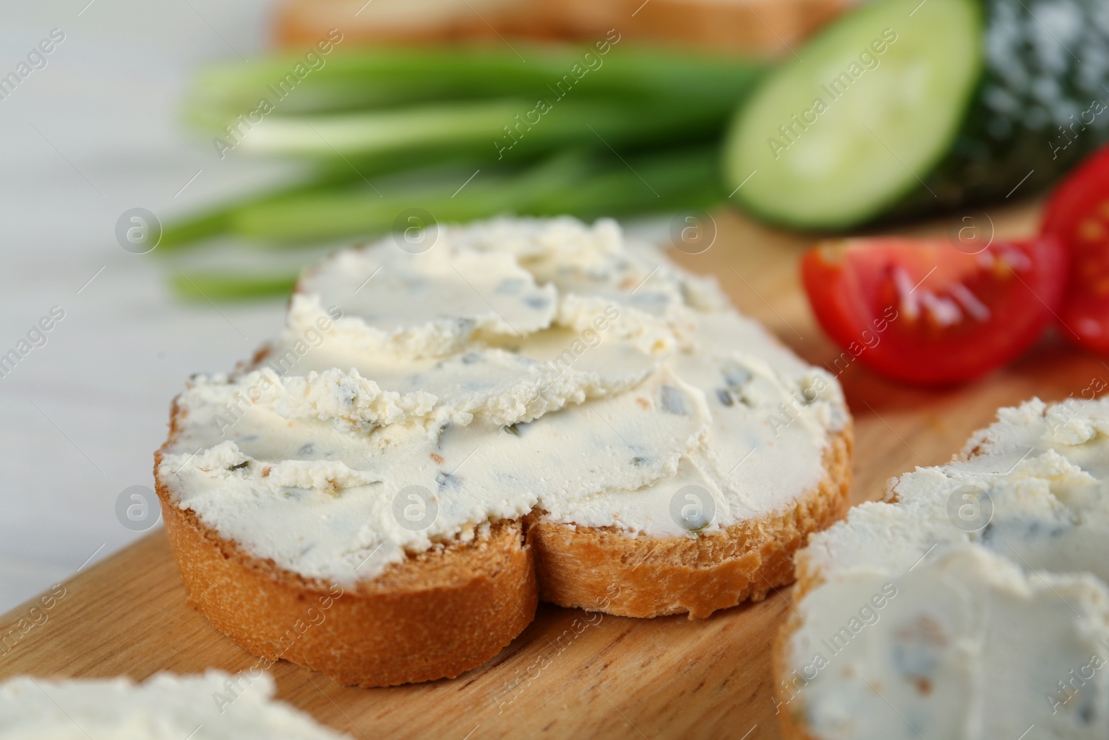 Photo of Toasted bread with cream cheese on wooden board, closeup