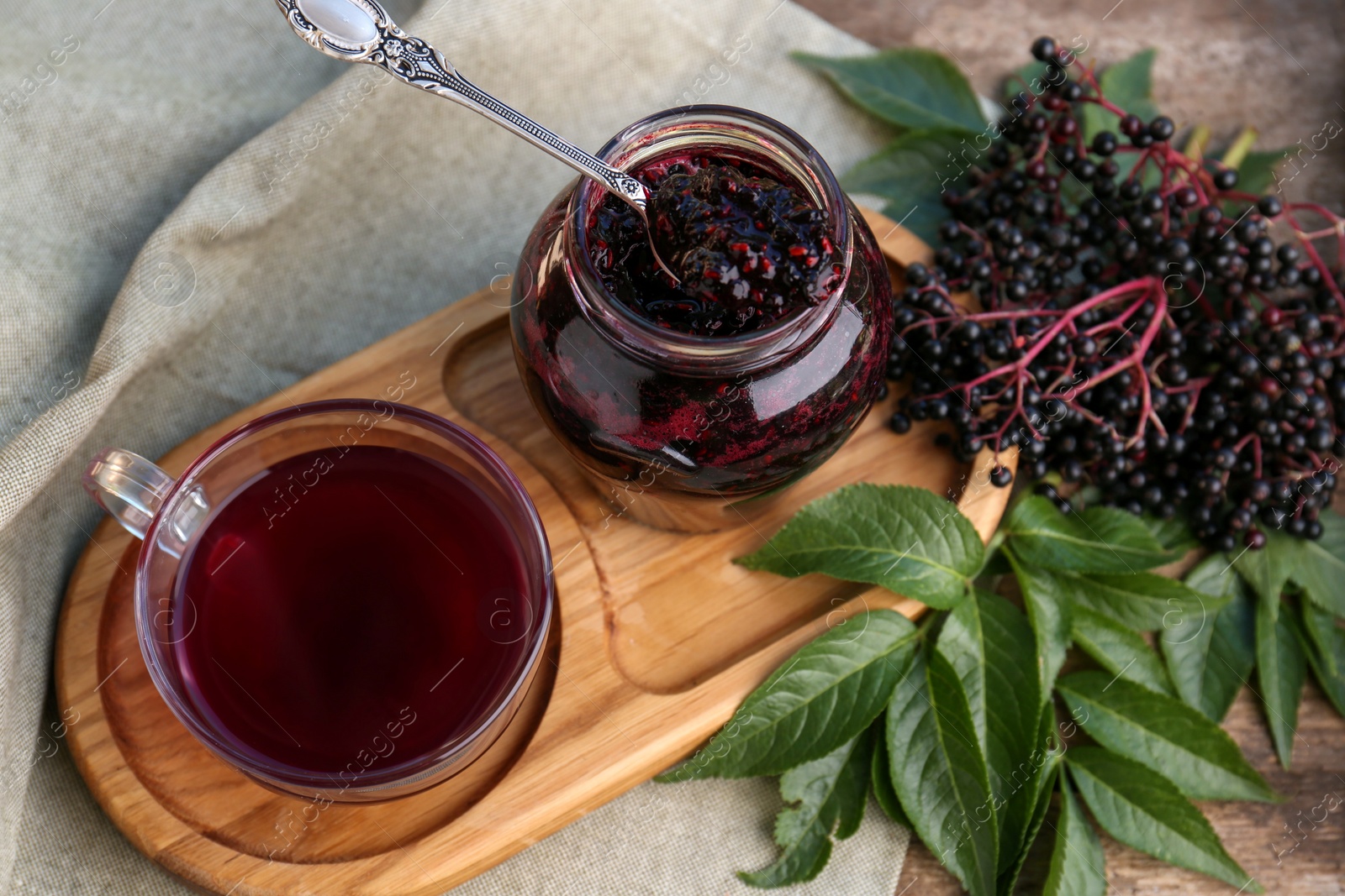 Photo of Elderberry jam, glass cup of tea and Sambucus berries on table, above view