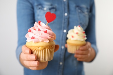 Photo of Woman holding tasty cupcakes for Valentine's Day on light background, closeup