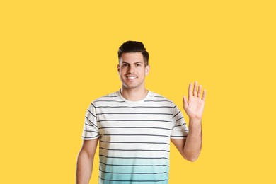 Cheerful man waving to say hello on yellow  background