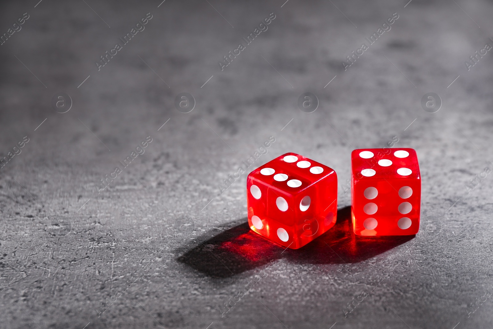 Photo of Two red game dices on grey textured table. Space for text