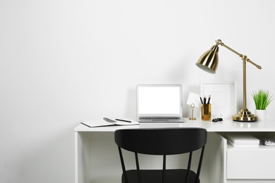 Cozy workspace with laptop, lamp and stationery on wooden desk at home. Space for text