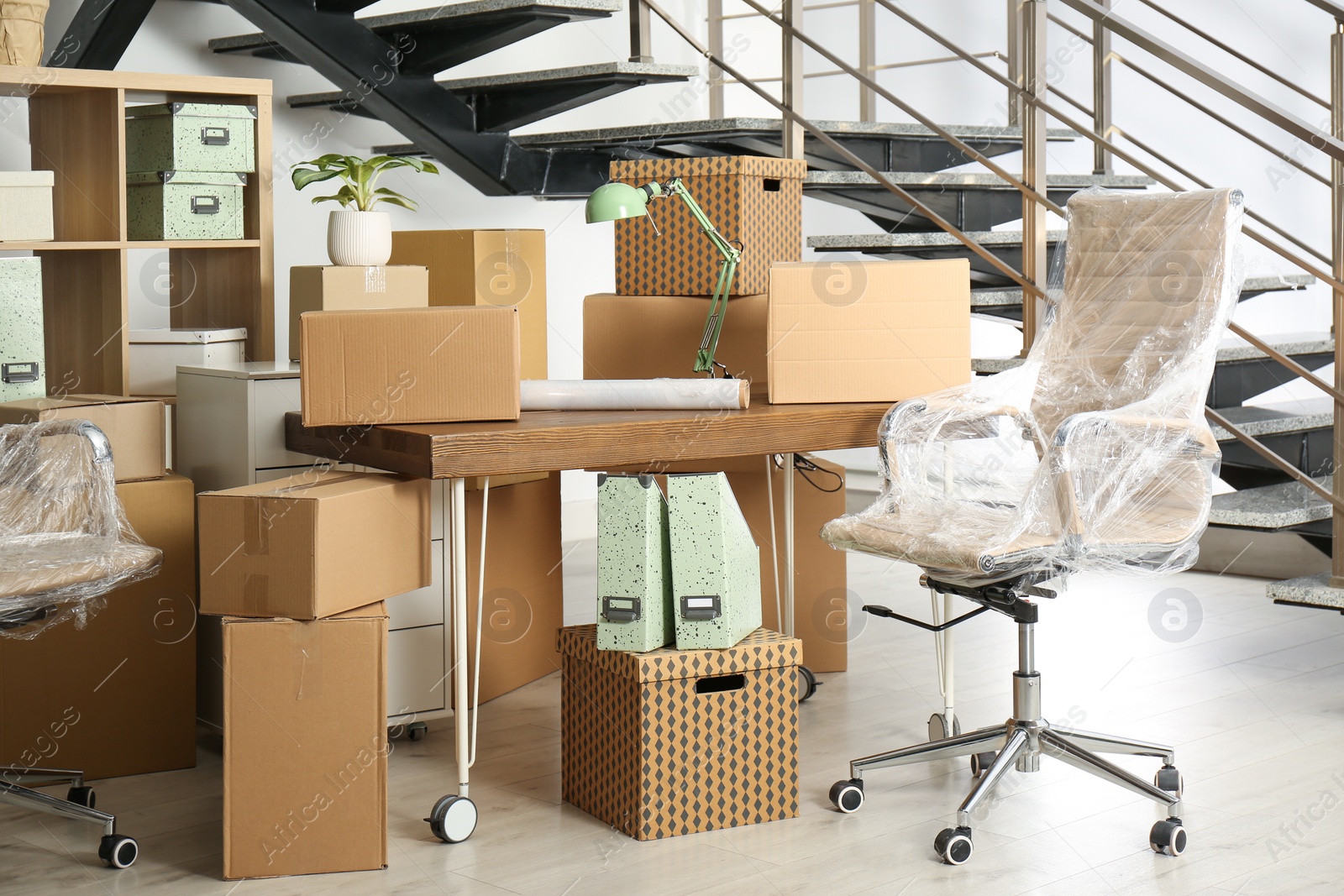 Photo of Cardboard boxes and furniture near stairs in office. Moving day