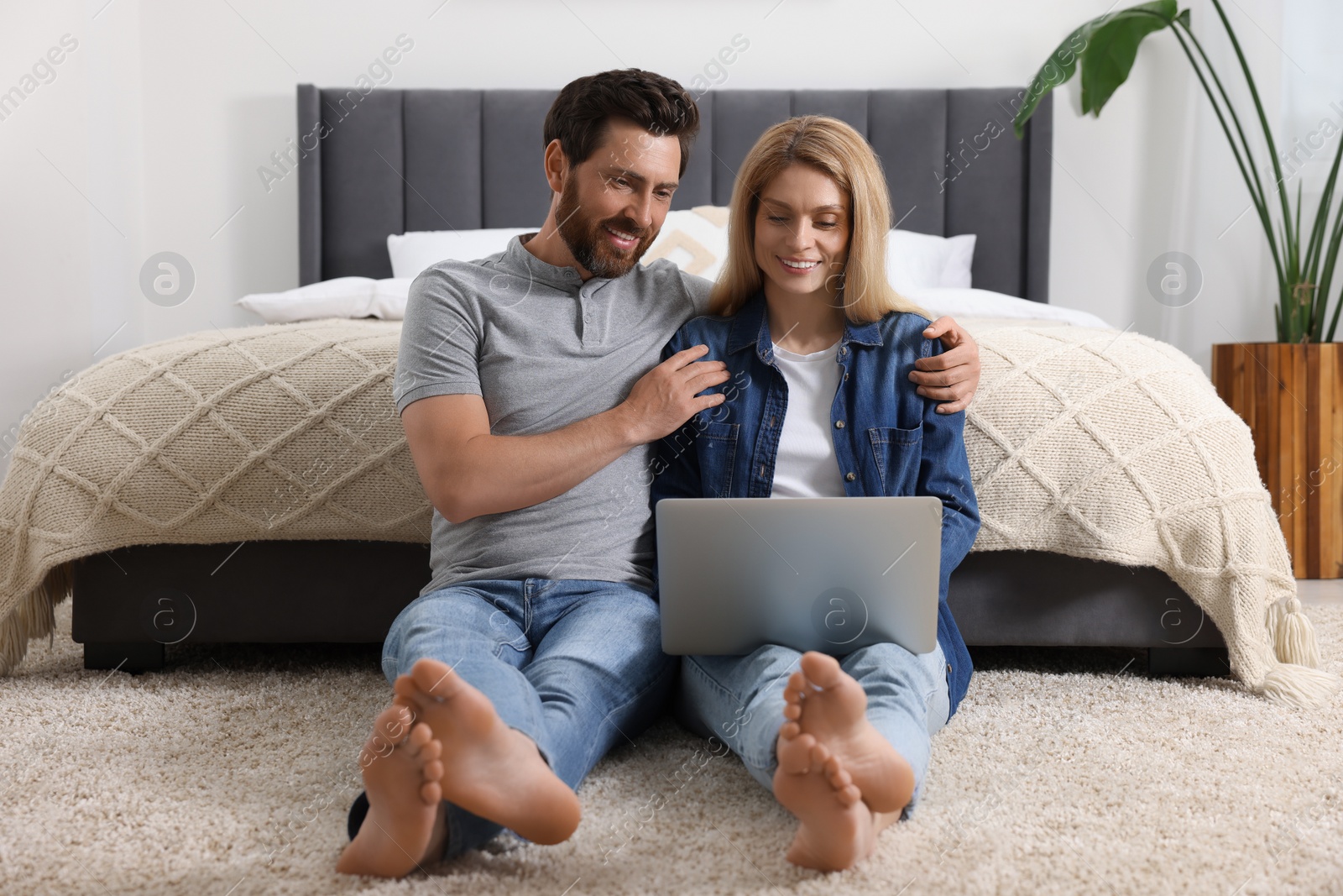 Photo of Happy couple with laptop on floor in bedroom