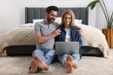 Photo of Happy couple with laptop on floor in bedroom