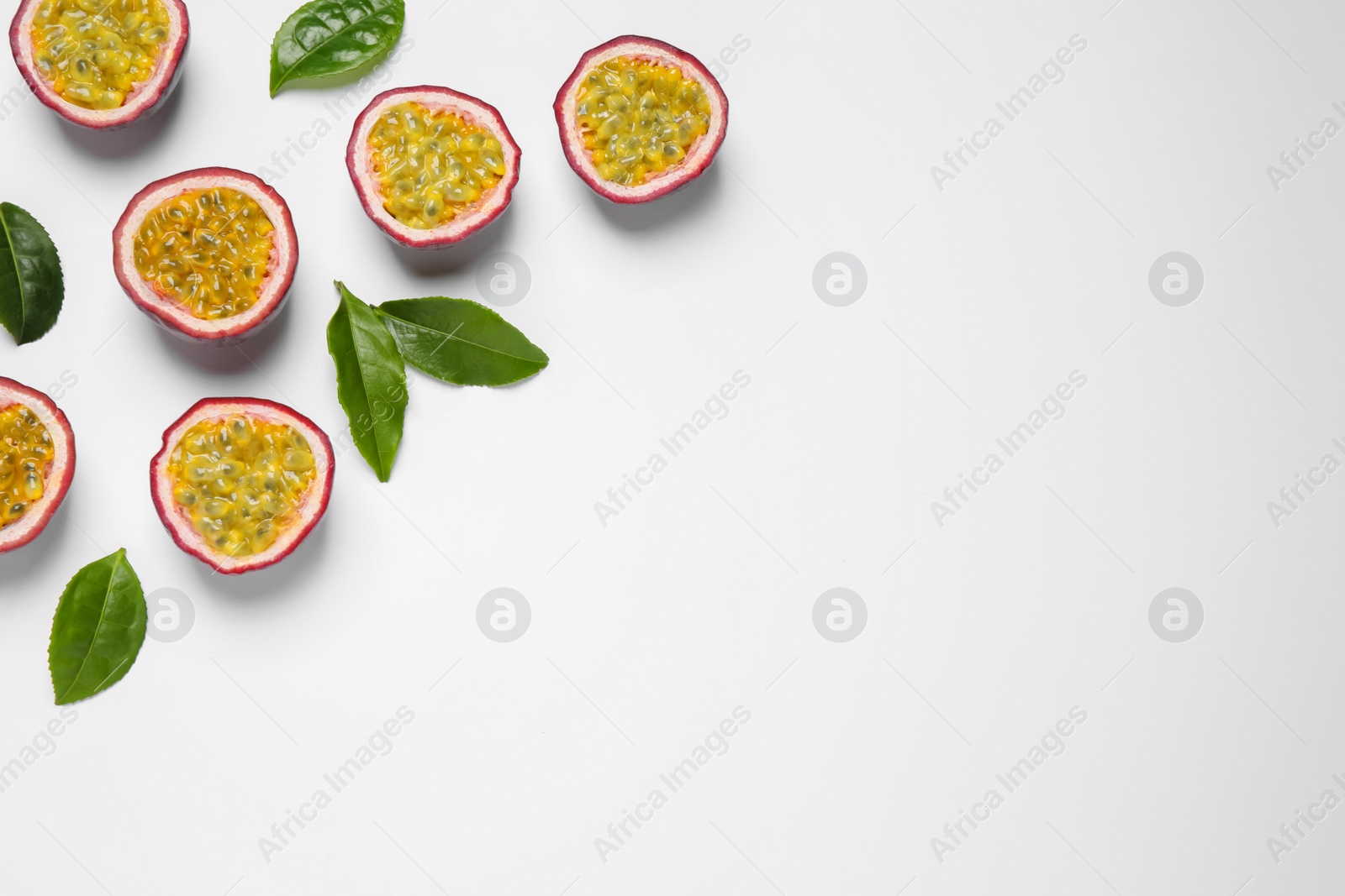 Photo of Halves of passion fruits (maracuyas) and green leaves on white background, flat lay. Space for text