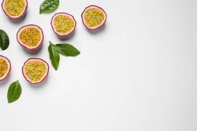 Halves of passion fruits (maracuyas) and green leaves on white background, flat lay. Space for text