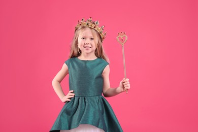 Photo of Cute girl in fairy dress and golden crown holding magic wand on pink background. Little princess