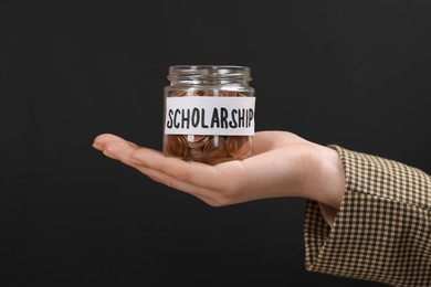 Photo of Woman holding glass jar with coins against black background, closeup. Scholarship concept