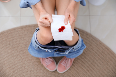 Photo of Woman holding toilet paper with blood stain in rest room, closeup. Hemorrhoid concept