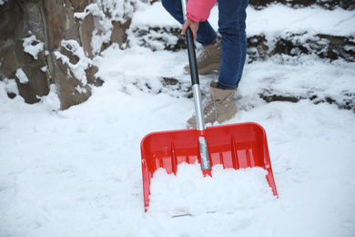 Woman cleaning snow with shovel outdoors on winter day, closeup