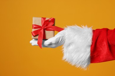 Photo of Santa Claus holding Christmas gift on orange background, closeup