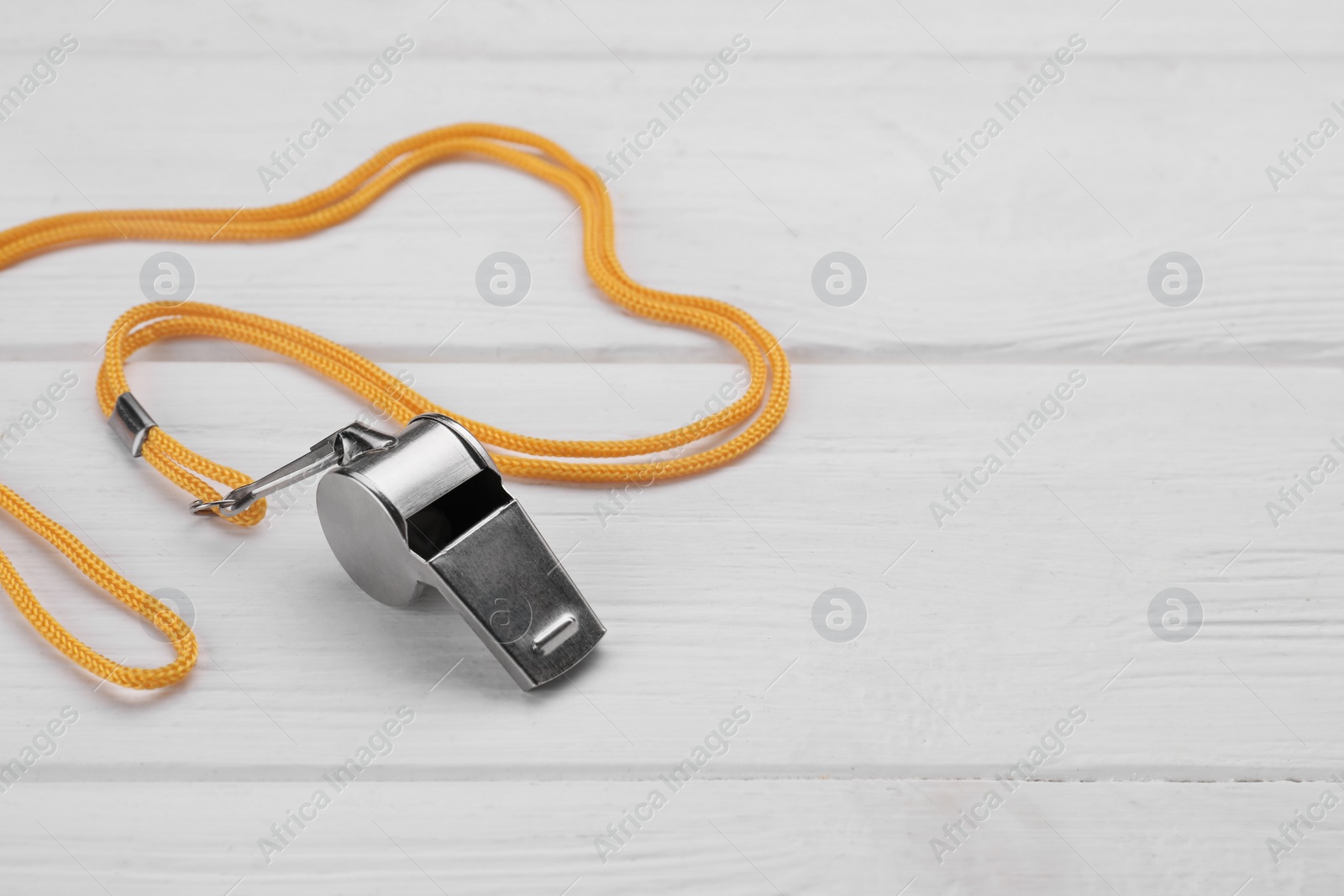 Photo of One metal whistle with cord on white wooden table. Space for text