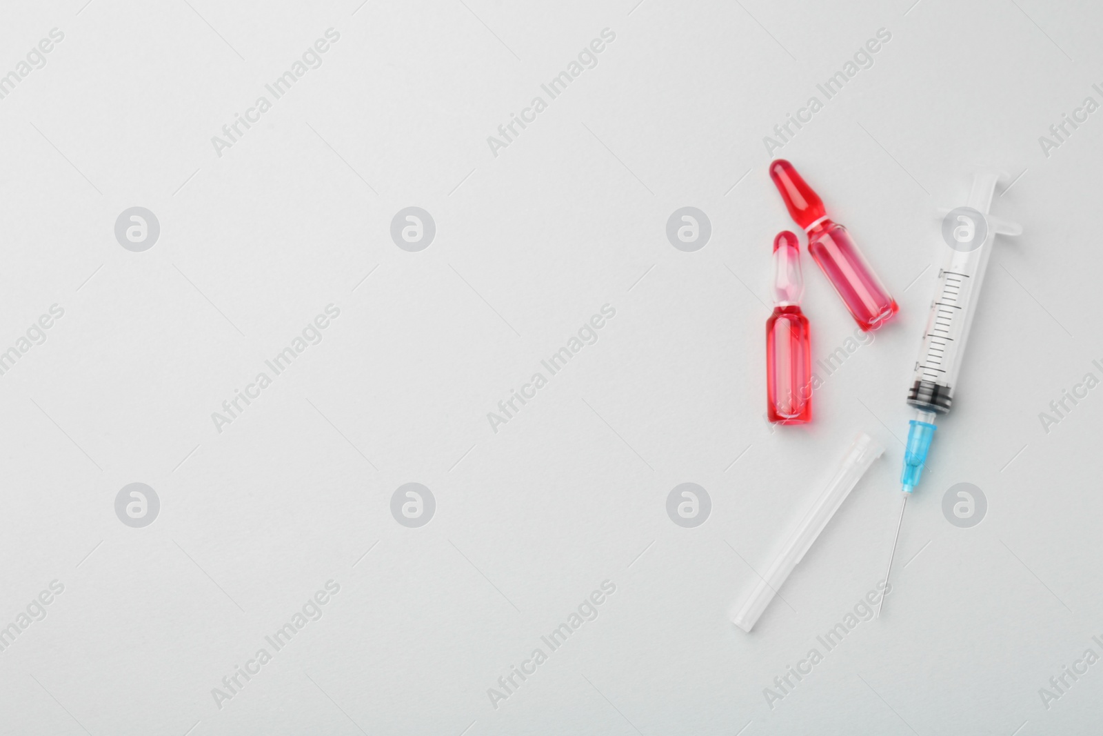 Photo of Glass ampoules with liquid and syringe on white background, flat lay. Space for text